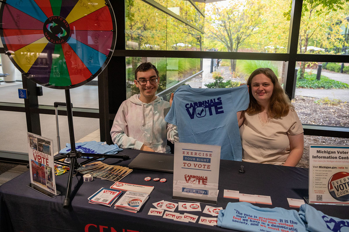 A male and a female college student sitting at a table filled with voting materials
